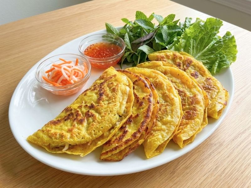 Golden crispy banh xeo filled with pork, shrimp, and bean sprouts served with fresh herbs