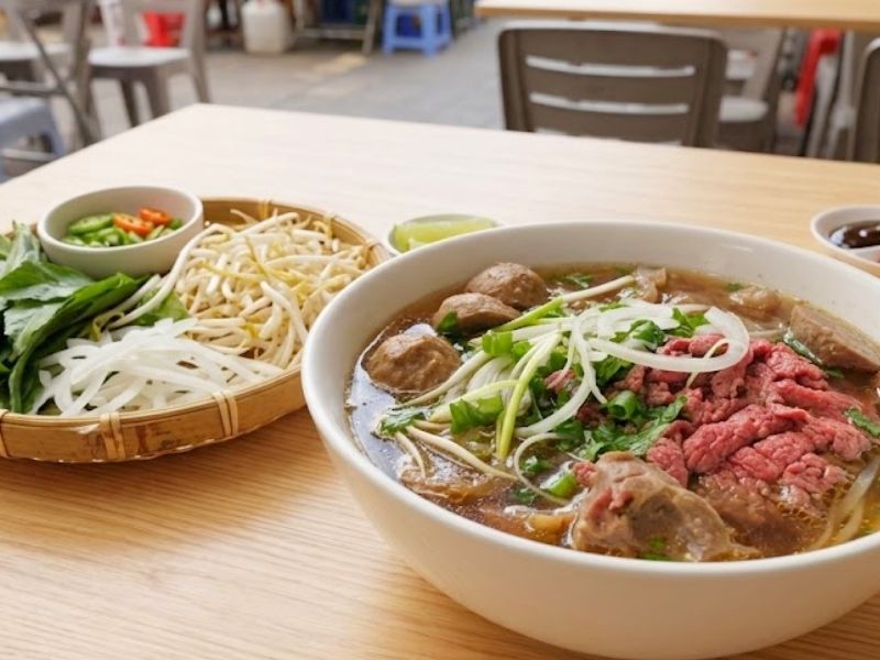 Vietnamese pho bo with clear beef broth, flat rice noodles, sliced beef, herbs, and aromatic spices