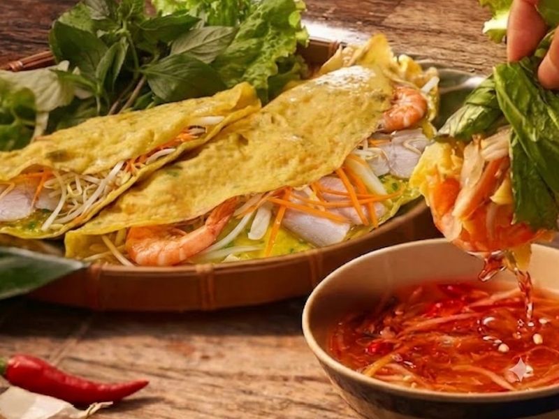 Serving banh xeo wrapped with lettuce, fresh herbs, pickled vegetables, and fish sauce dipping sauce