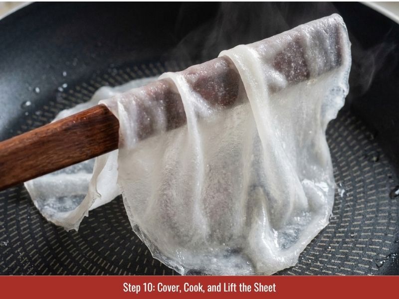 Covering the skillet and lifting cooked translucent banh cuon rice sheets