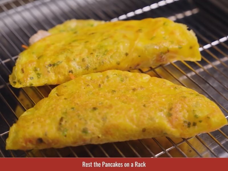 Resting cooked banh xeo on a wire rack to preserve the crispy texture