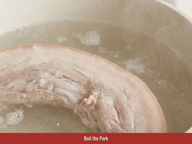 Boiling pork belly with shallot, salt, and sugar to prepare filling for Vietnamese fresh spring rolls