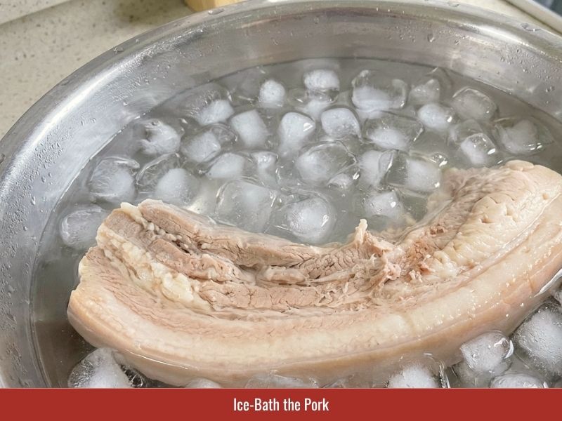 Cooling cooked pork belly in an ice bath to firm the meat before slicing