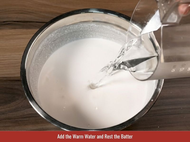 Mixing warm water into banh uot batter and resting it overnight for softer rice sheets