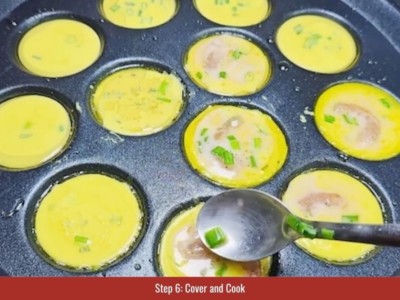 Covering the banh khot pan while the mini pancakes cook until the batter sets and edges crisp