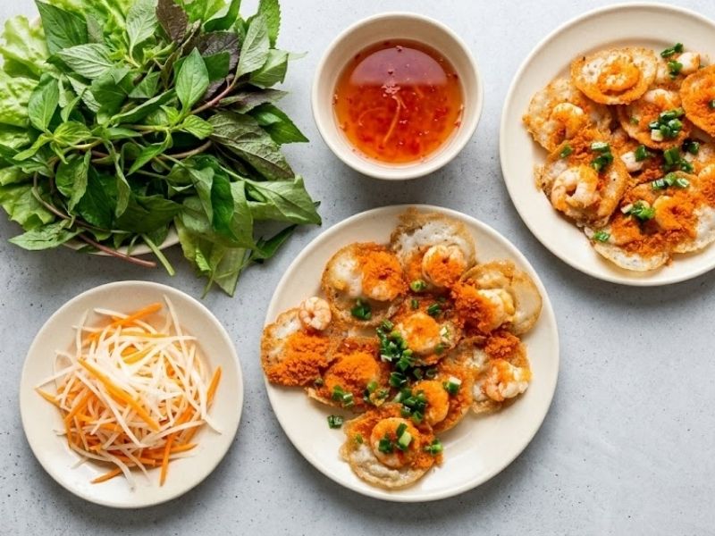 Plate of crispy banh khot with shrimp, coconut rice batter, lettuce, herbs, and nuoc cham