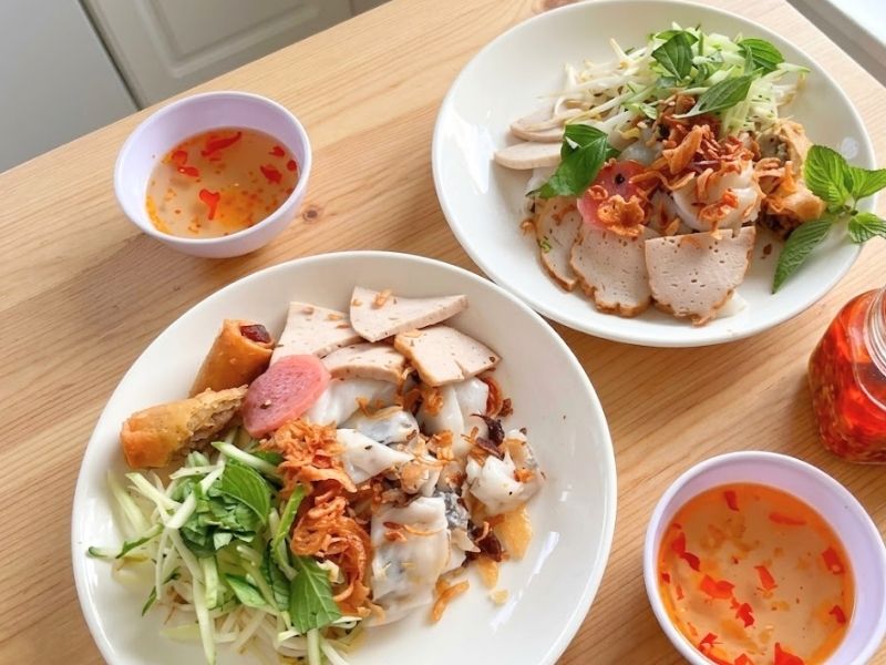 Plate of soft Vietnamese banh uot rice sheets topped with cha lua, fried shallots, fresh herbs, and nuoc cham
