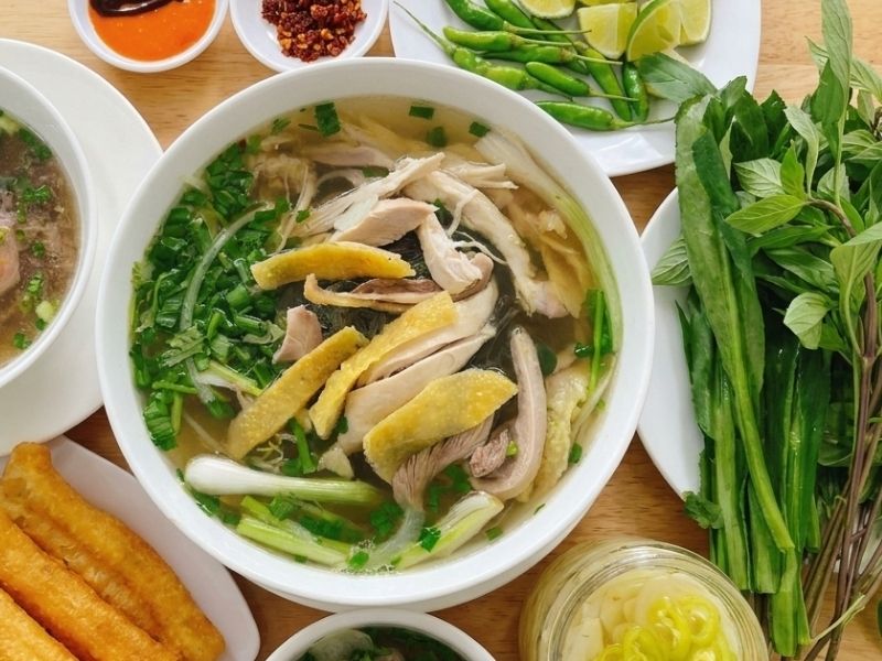Bowl of phở gà with tender chicken, clear aromatic broth, rice noodles, green onion, herbs, and black pepper